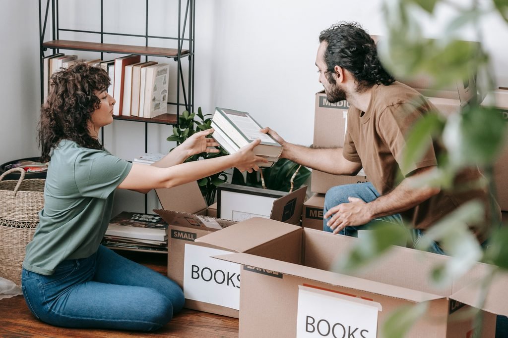 Two people sorting books and household items into boxes.